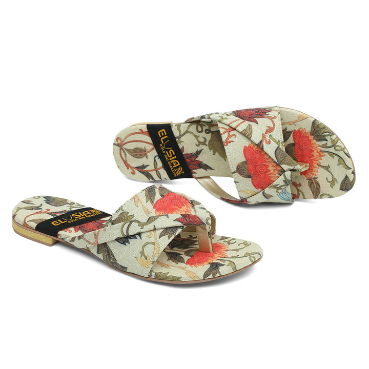 A pair of multicolor floral printed slippers with a label that reads 'the elysian'.