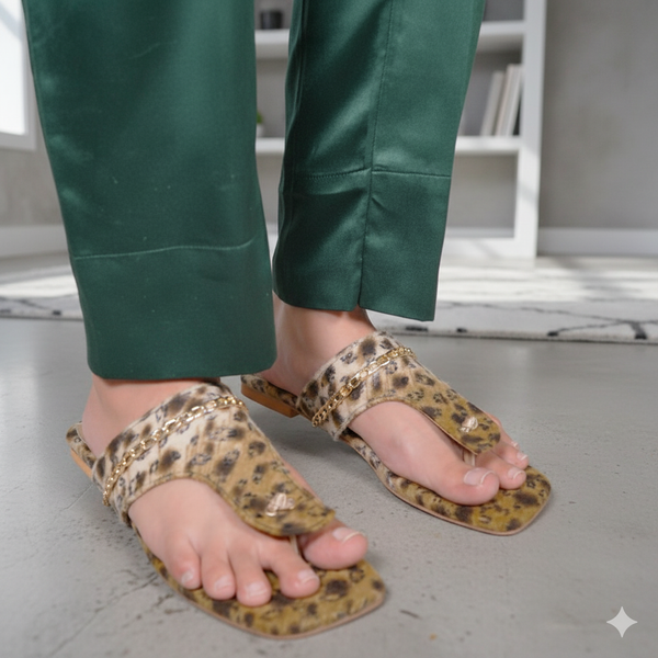Person wearing leopard print sandals with gold accents and green pants on a light gray floor.